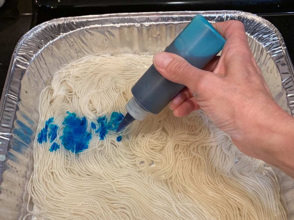 image of a hand applying blue dye to yarn with a squeeze bottle